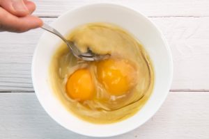 ตอกไข่ไก่ลงในน้ำแกงเขียวหวานที่แยกไว้ ตามด้วยน้ำเปล่า ตีให้เข้ากัน